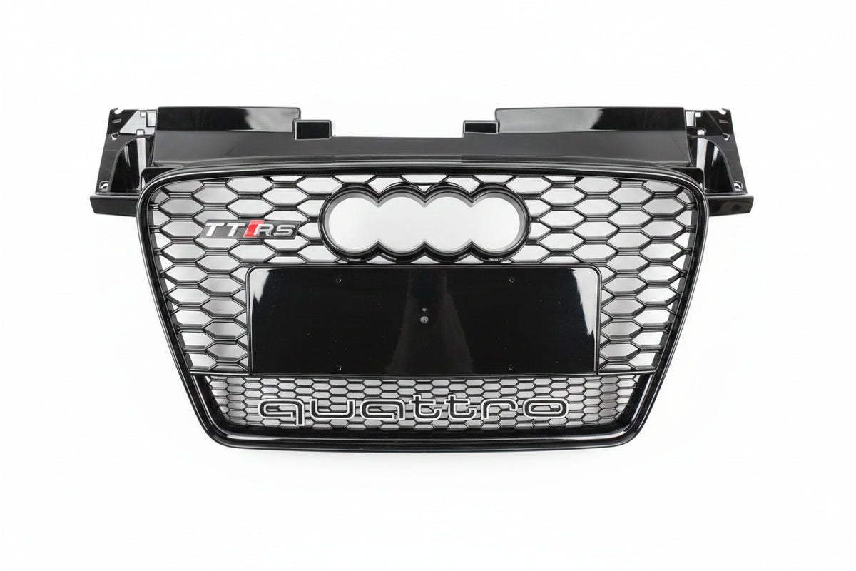 A glossy black Audi Q5 TFS quattro front grille with the four-ring logo and 'quattro' text, photographed from above on a gray asphalt surface.