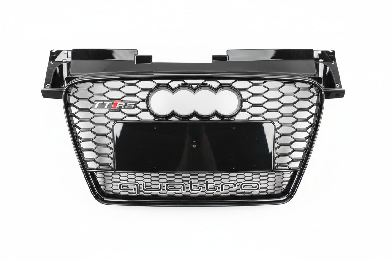 A glossy black Audi Q5 TFS quattro front grille with the four-ring logo and 'quattro' text, photographed from above on a gray asphalt surface.